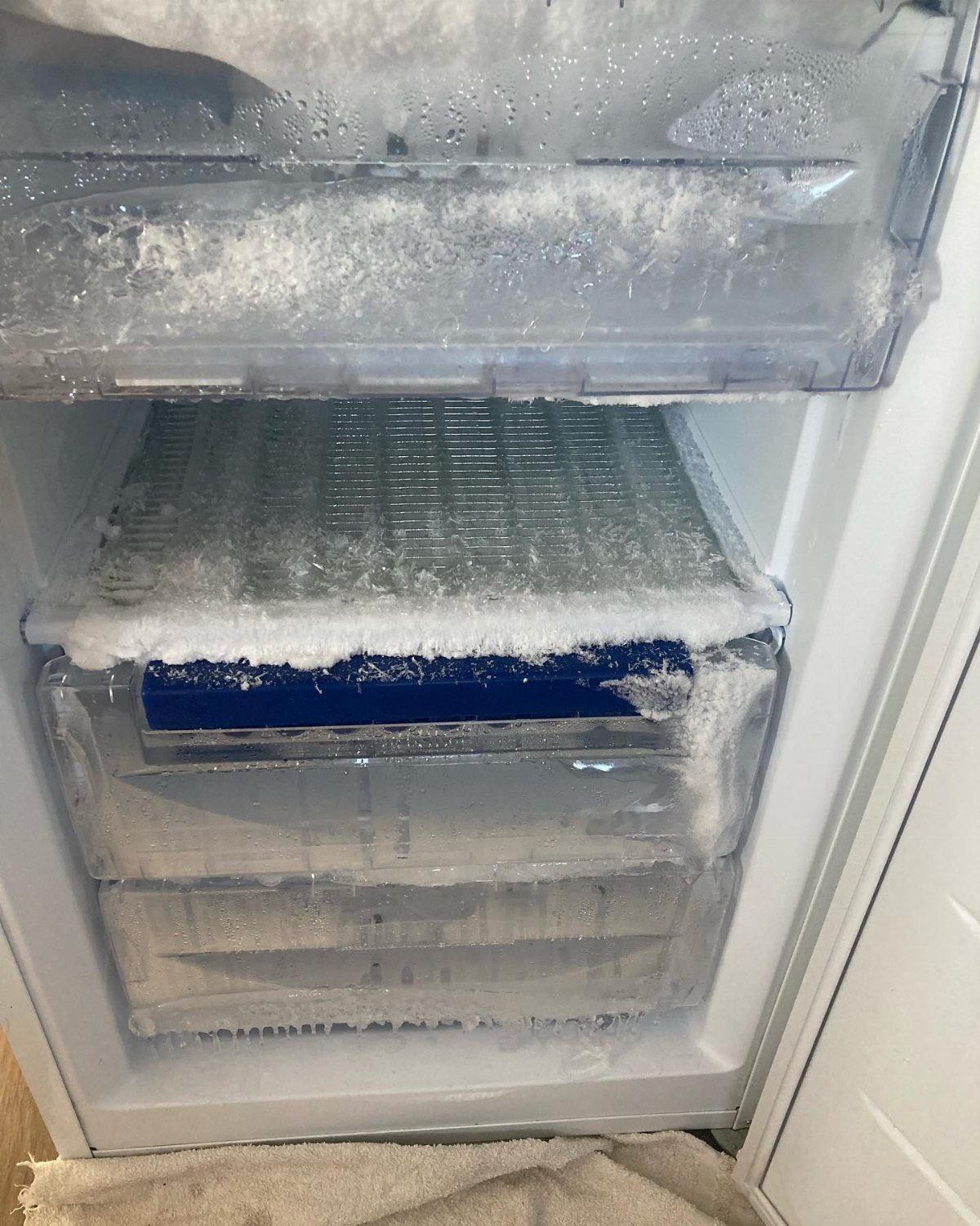 Frost and ice buildup covering the clear plastic drawers inside an open freezer.