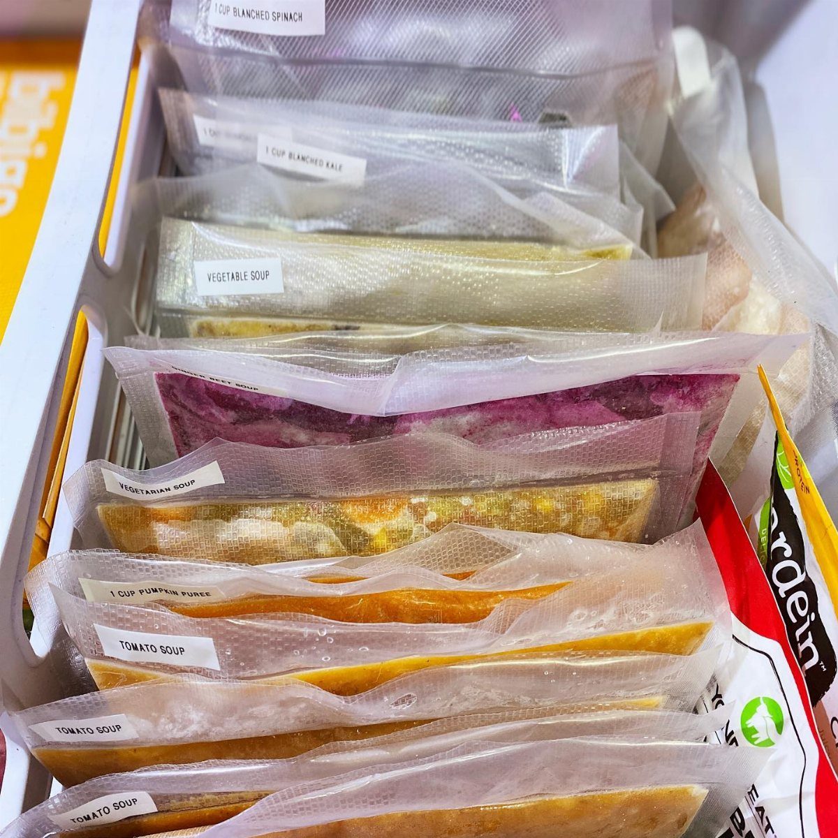 Frozen food bags labeled with contents stand vertically inside a white freezer drawer.