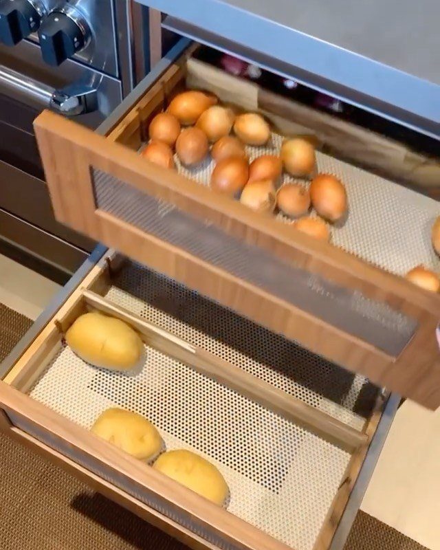Wooden ventilated produce drawers containing several potatoes pulled out from a kitchen cabinet.