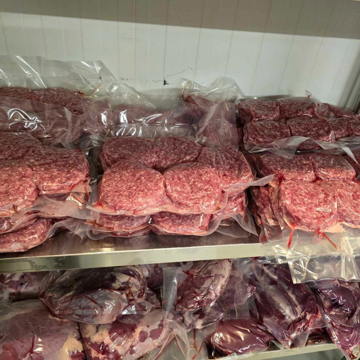Vacuum-sealed packages of raw red meat arranged on metal refrigerator shelves.