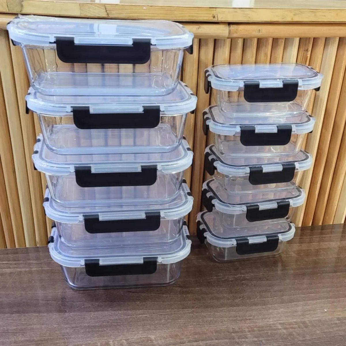 Two stacks of clear glass airtight containers with black lids on a wooden table.
