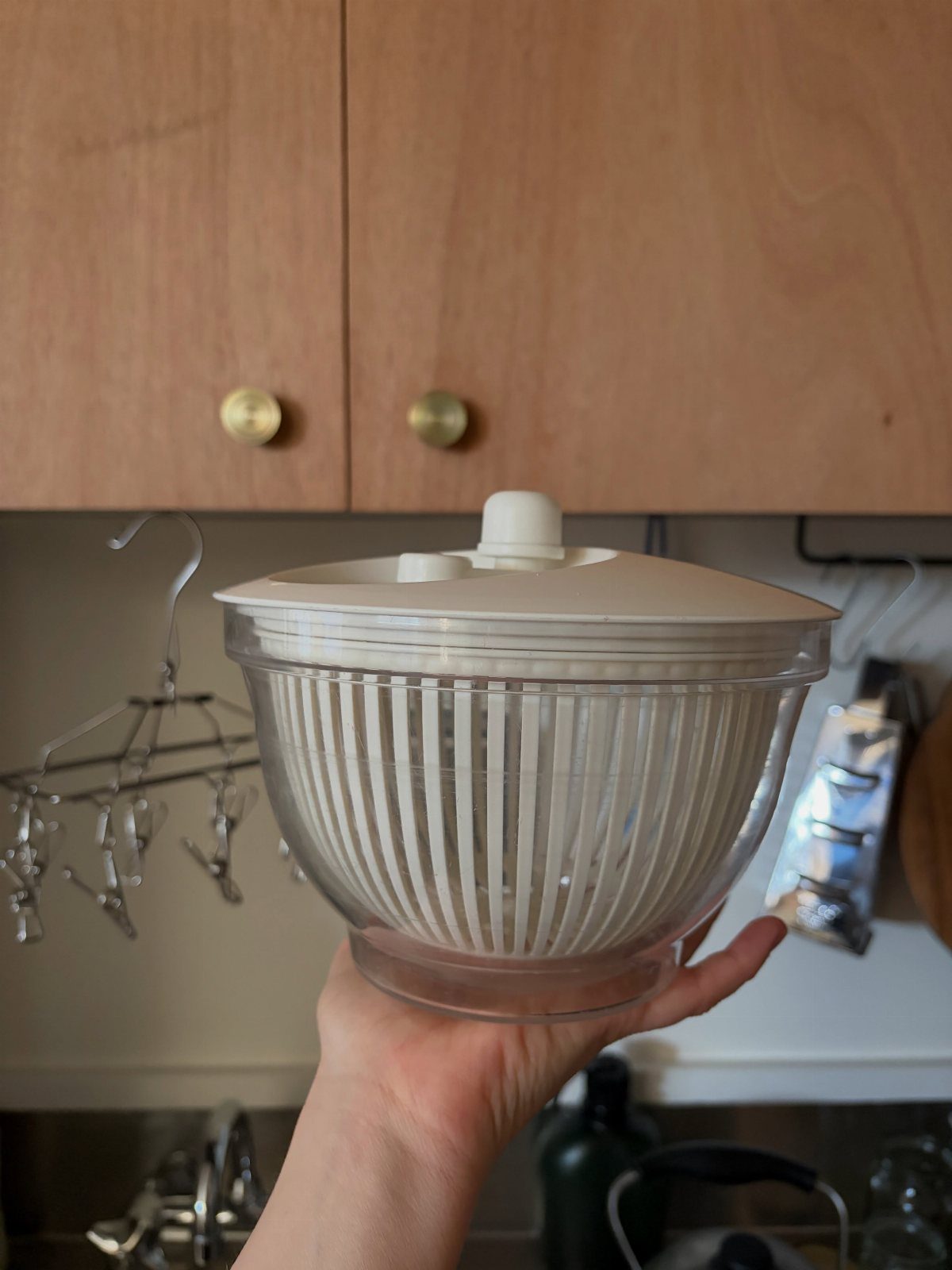 A hand holding a clear plastic salad spinner with a white inner basket.
