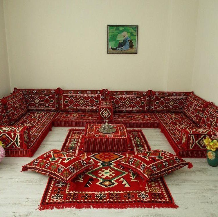 Red patterned floor cushions and pillows arranged around a central ottoman on layered rugs.
