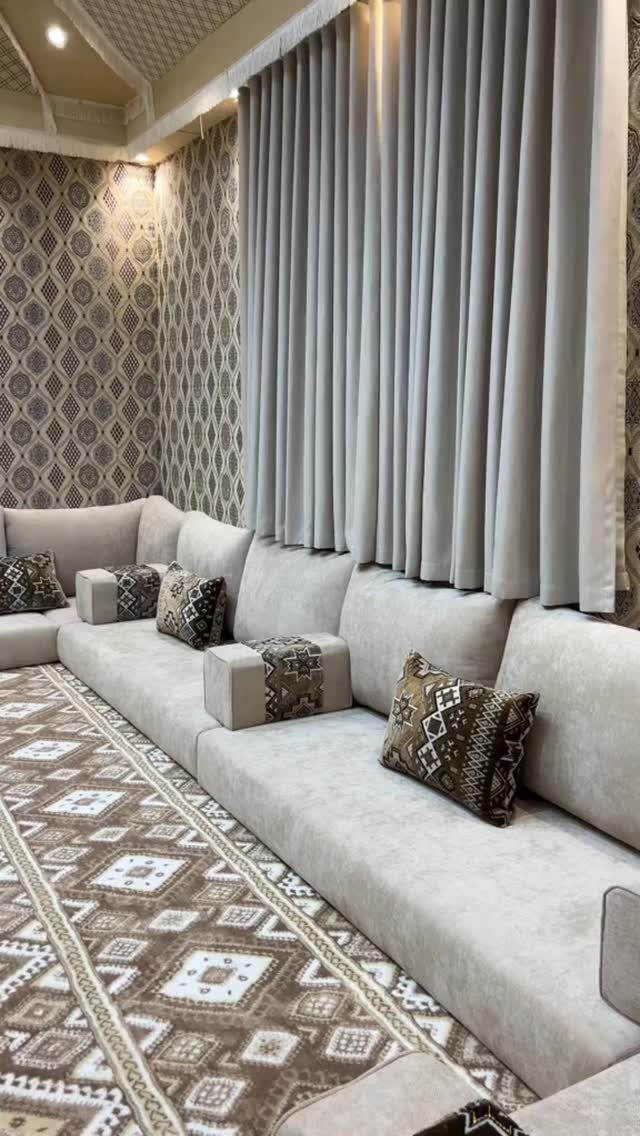 Beige low seating sofa arranged on a patterned rug with grey curtains and patterned wallpaper.