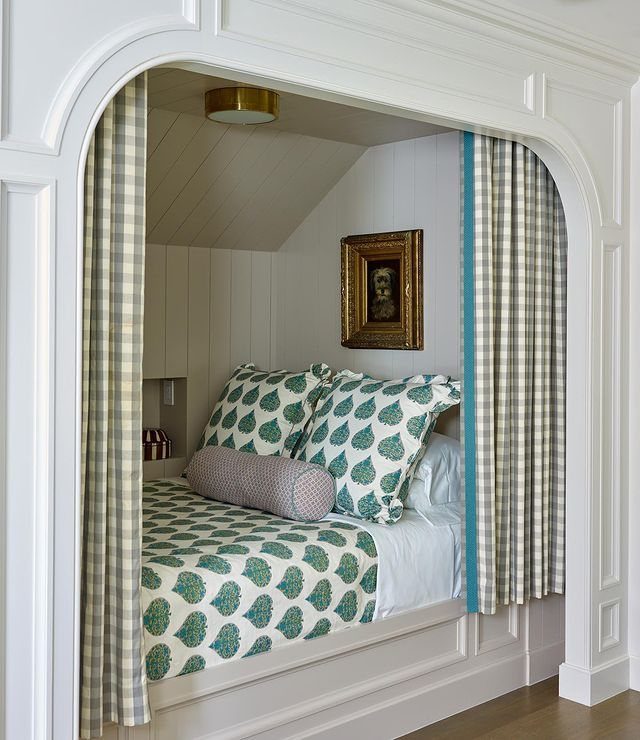 A built-in alcove bed with teal patterned bedding tucked inside a white arched wall nook.