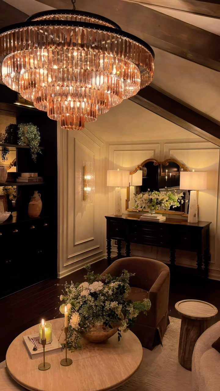 A large tiered crystal chandelier glowing warmly above a living area with candles and flowers.