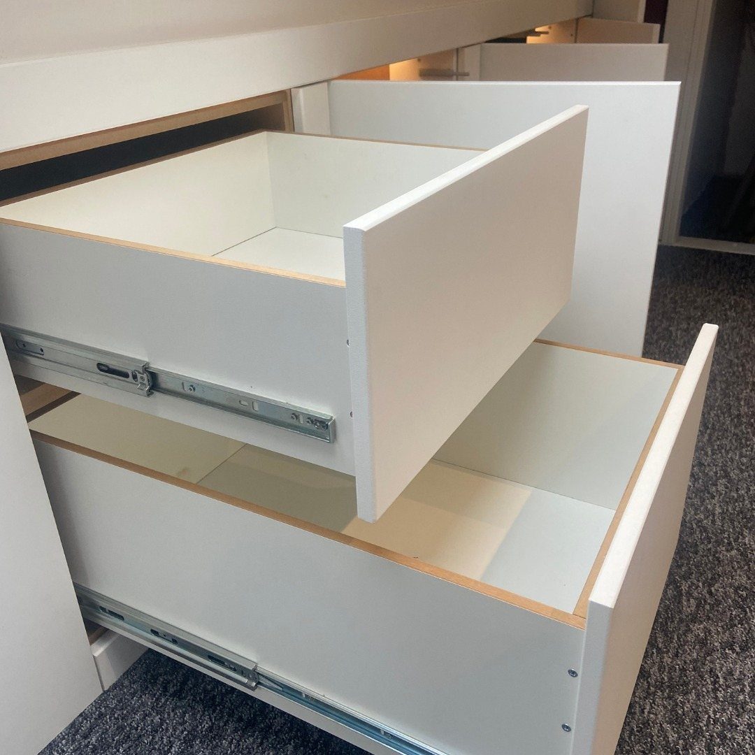 Open white wooden drawers with metal glides built into a storage unit.