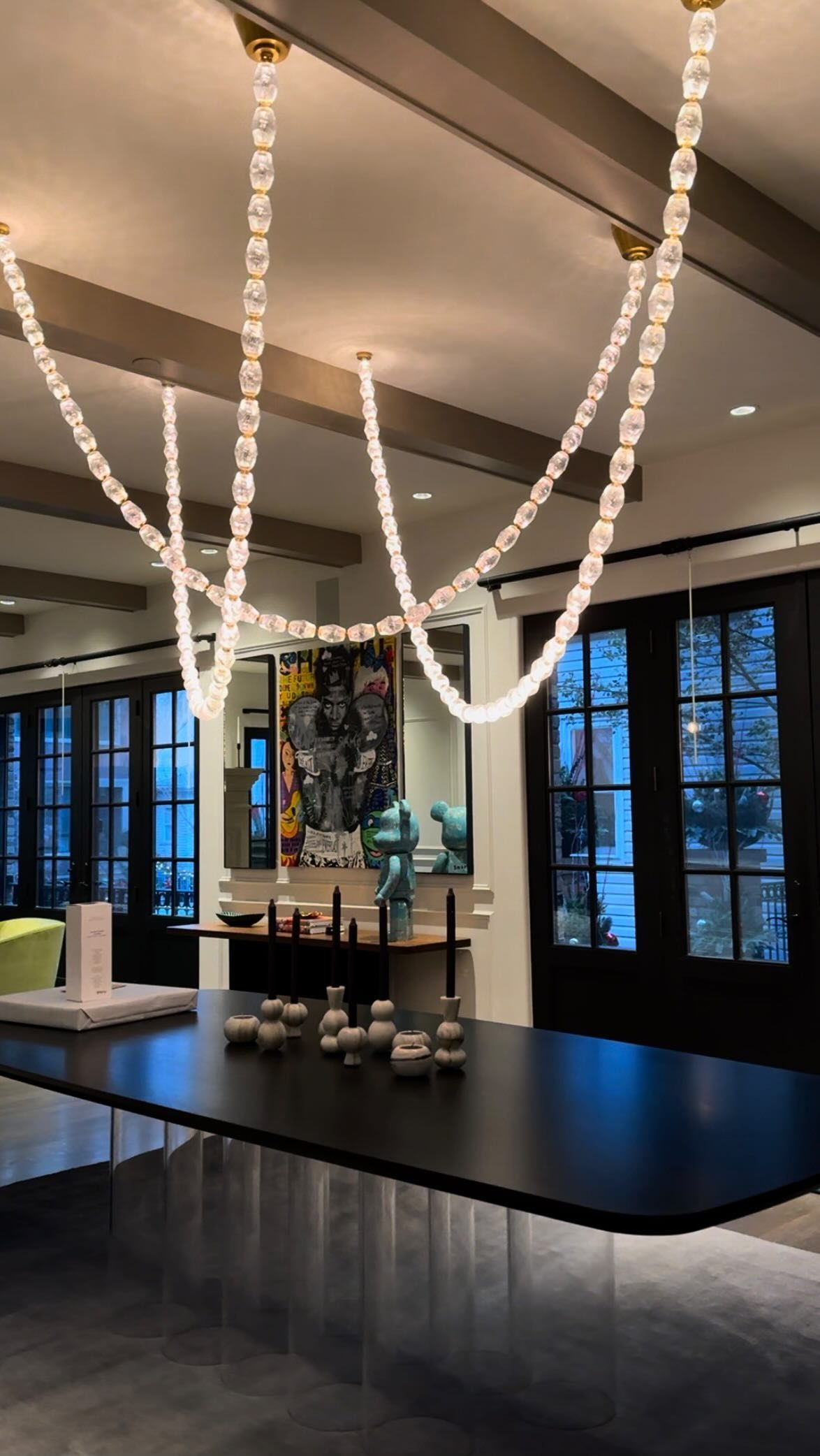 A modern chandelier with glowing oval links hangs above a long black dining table.