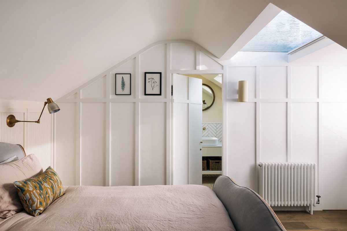 A bright attic bedroom with white paneled walls and a large skylight in the ceiling.