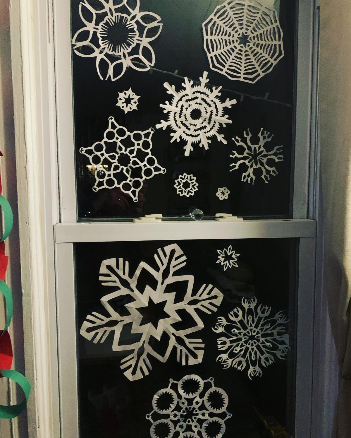 White paper snowflakes of various intricate patterns displayed on a dark glass window pane.