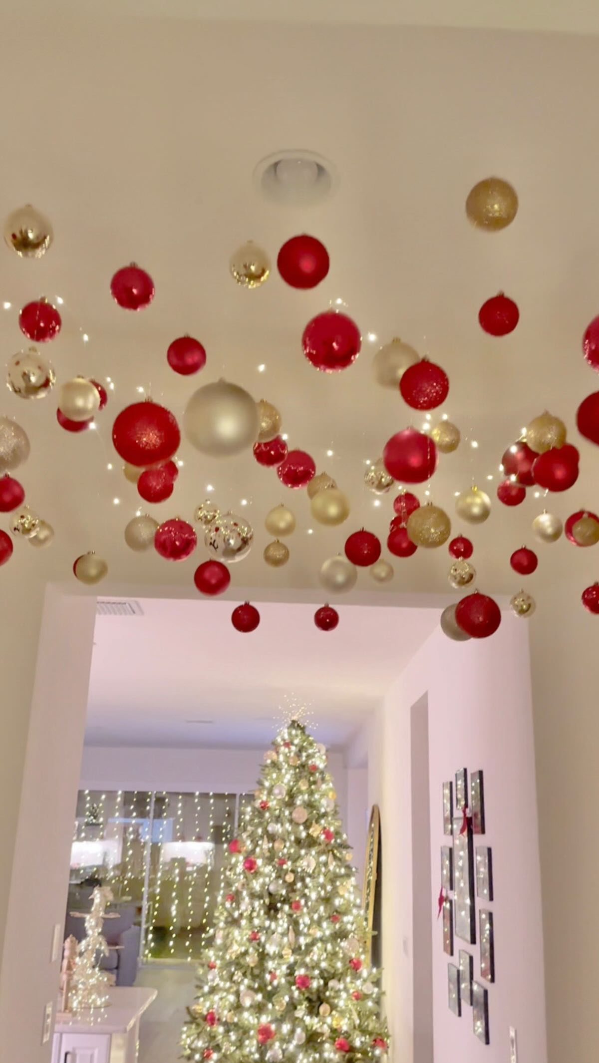Red and gold Christmas ornaments hanging from a white ceiling above an open doorway.