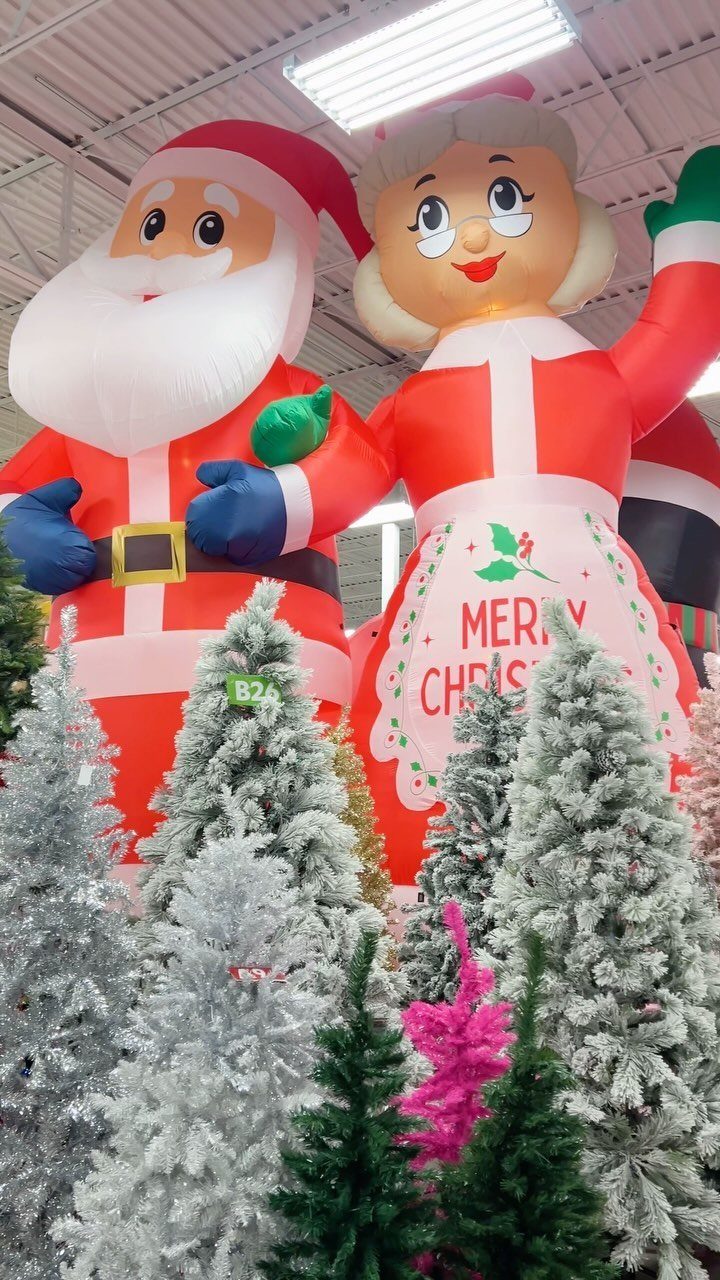 Large inflatable Santa and Mrs. Claus figures standing behind small frosted Christmas trees.