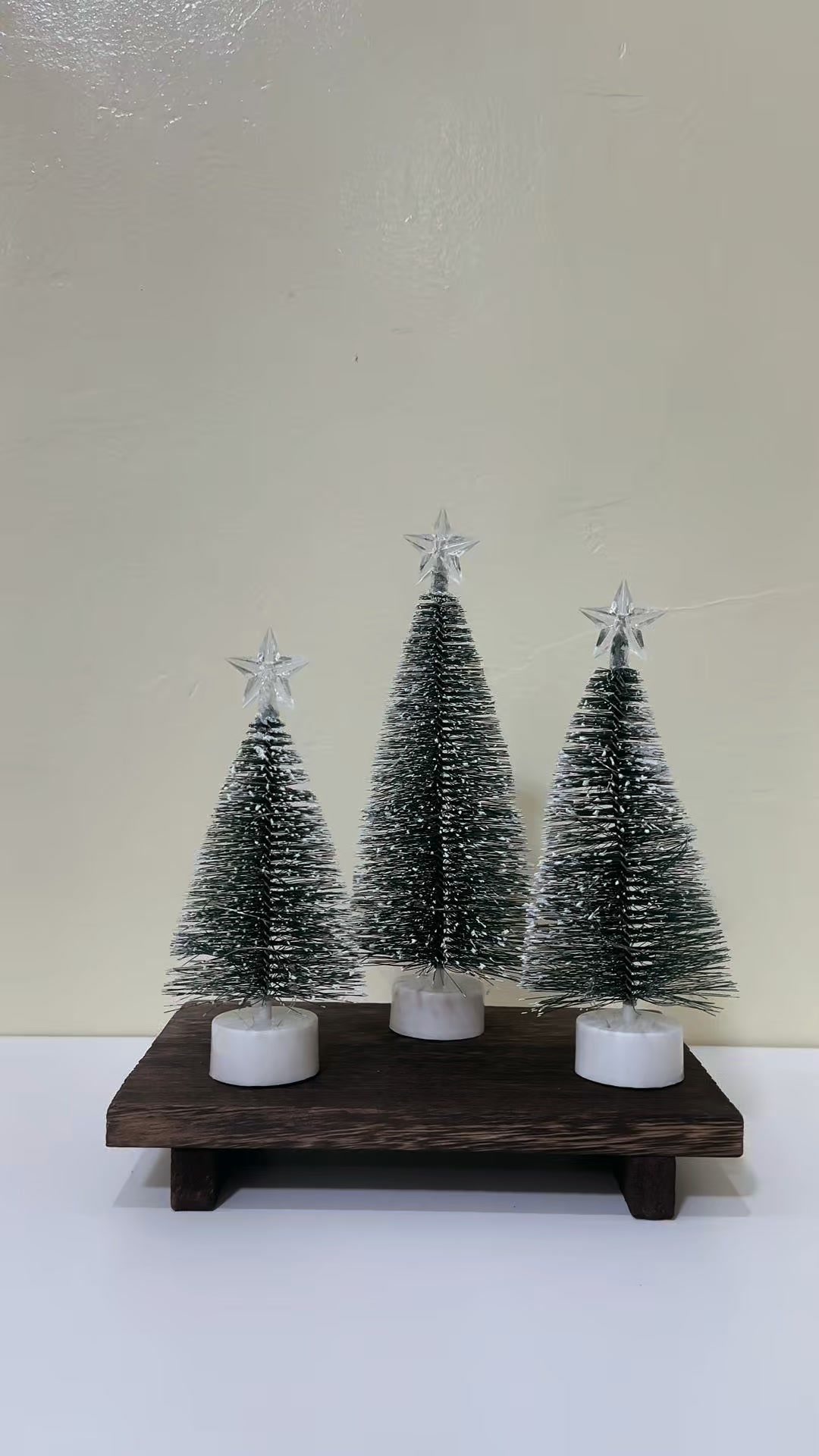 Three small flocked mini Christmas trees with silver stars on a wooden base.