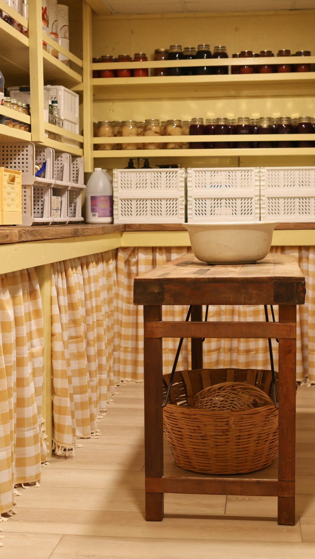 Glass jars of preserved food arranged on yellow shelves above a wooden pantry counter.