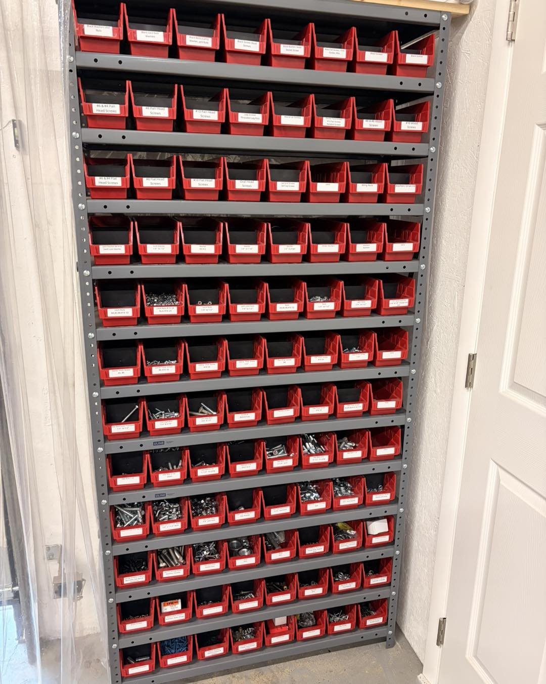 Red plastic storage bins with white labels organized on a tall grey metal shelving unit.