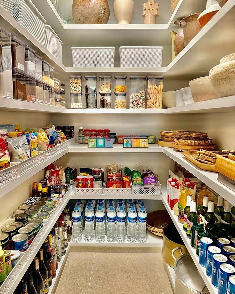 Organized white pantry shelves filled with grouped canned goods, bottled water, and clear containers of dry food.