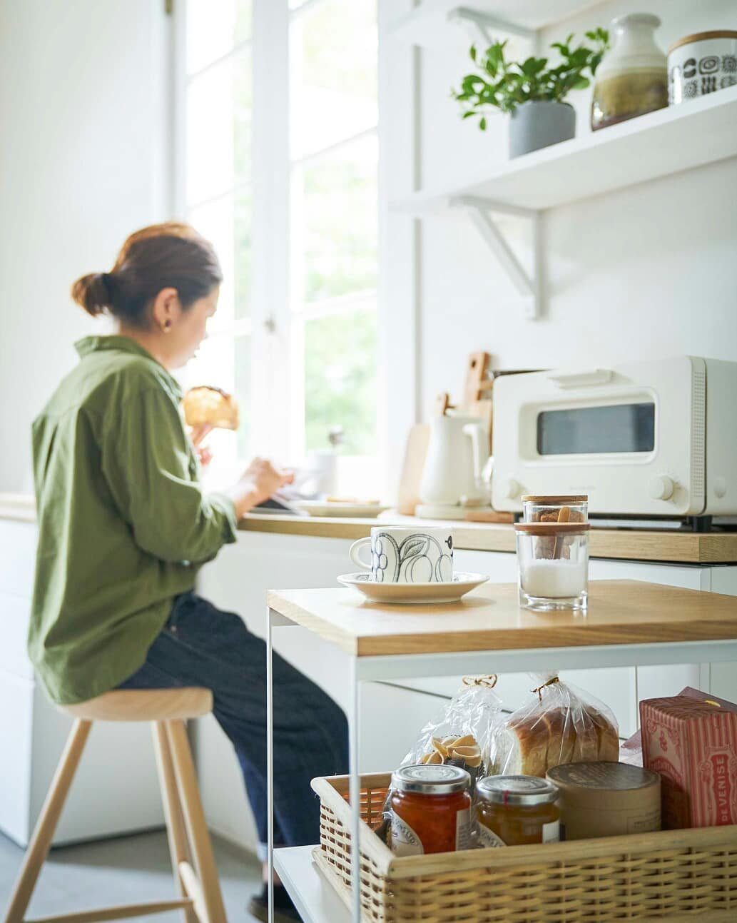A wooden rolling cart holding a wicker basket of food items in a bright kitchen.