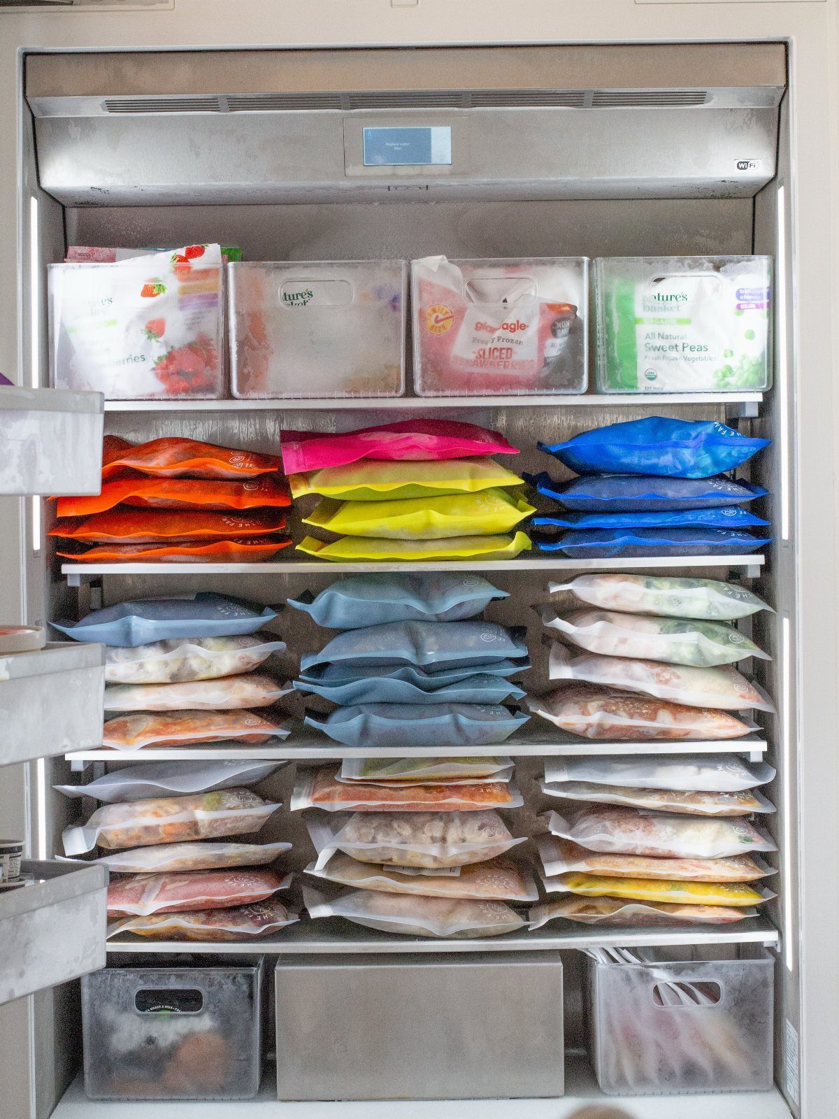 A stainless steel freezer filled with organized rows of colorful frozen food bags and clear containers.