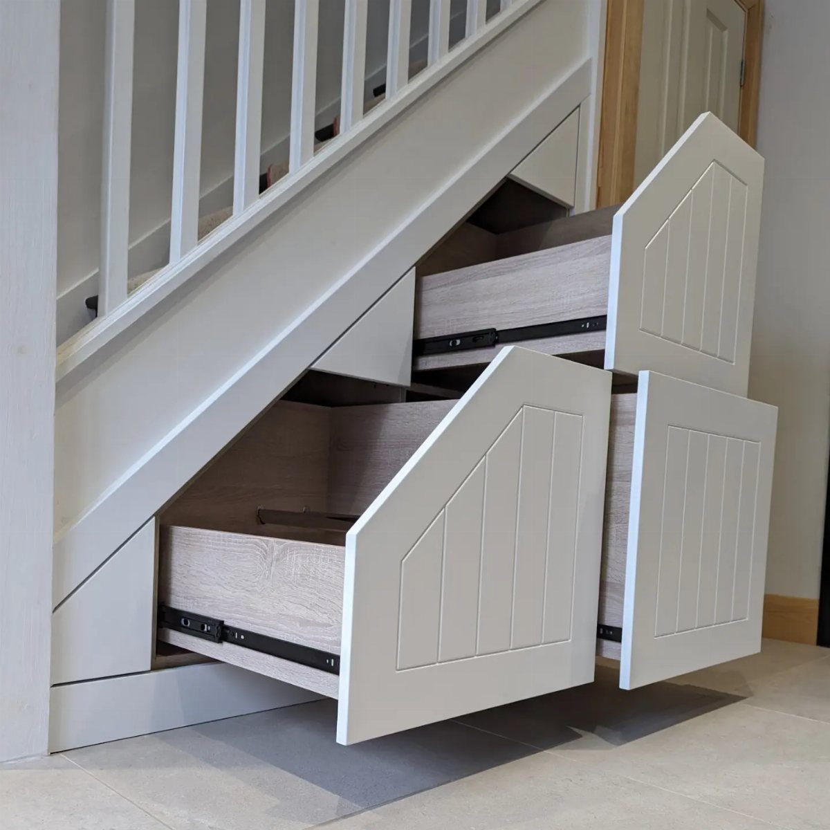 White paneled drawers pulled out from the storage space underneath a staircase.