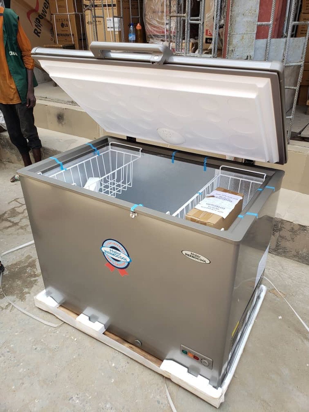 An open stainless steel chest freezer with wire baskets sitting on a white pallet.