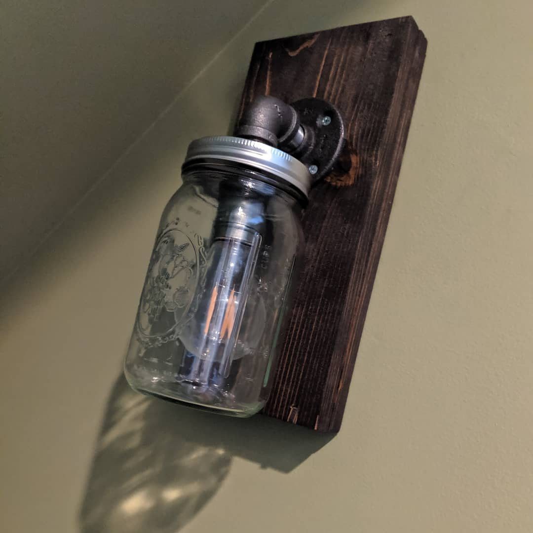 A mason jar wall sconce with an Edison bulb mounted on dark wood against a green wall.
