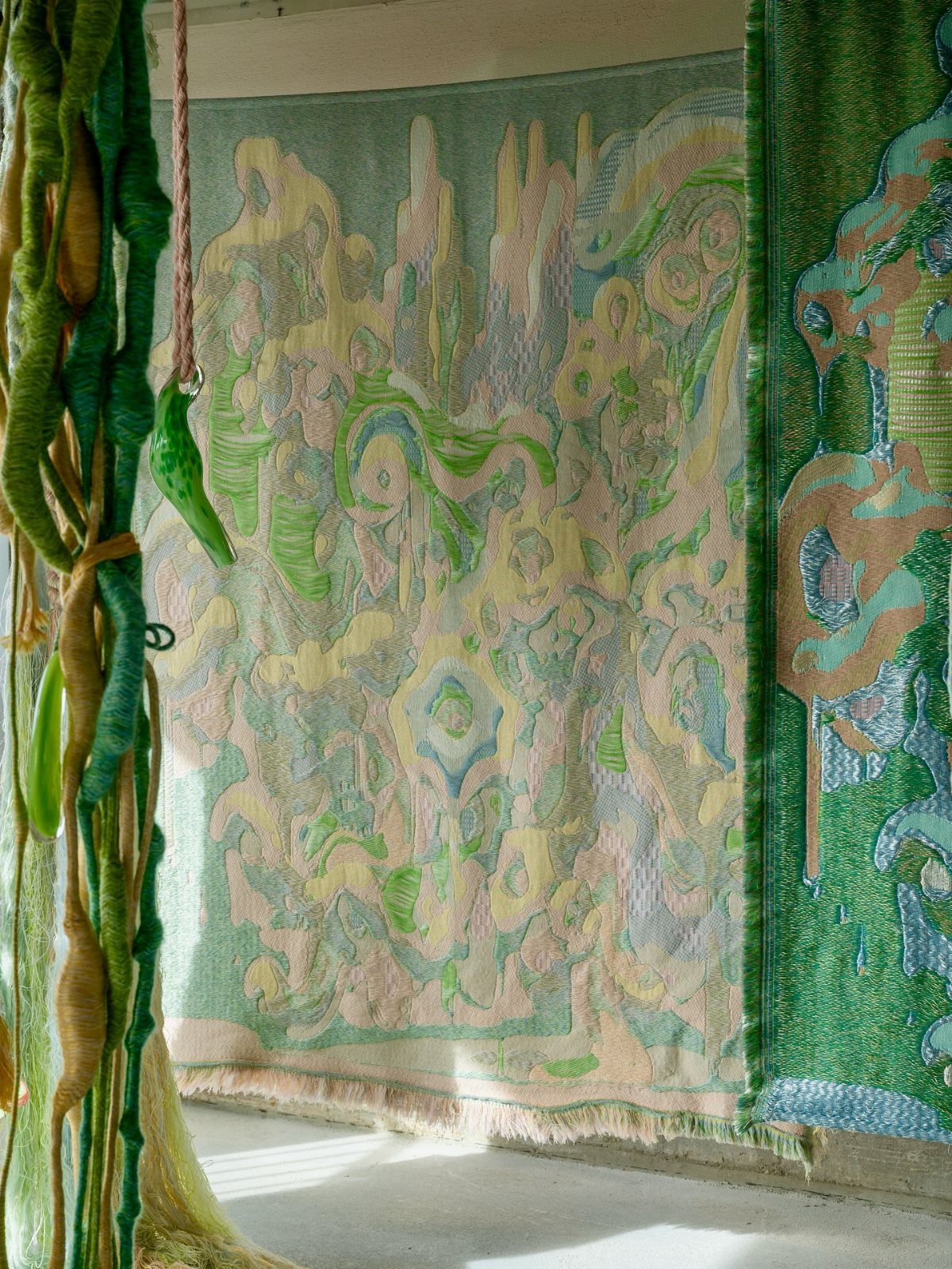 Large woven tapestries with abstract green and sandy beige ocean-inspired patterns hanging on a wall.