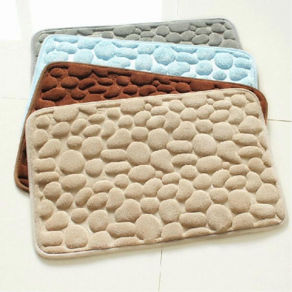 Four textured bath mats in grey, blue, brown, and beige stacked on a white floor.