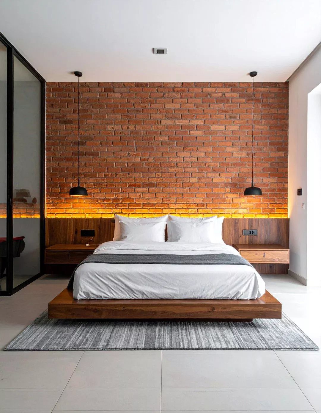 A modern bedroom with a red brick accent wall and a wooden platform bed.