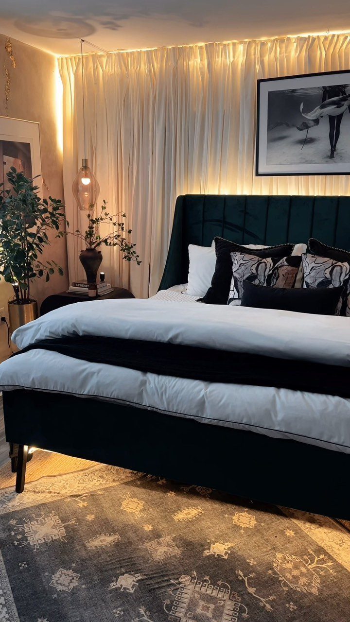 Dark green velvet bed with white bedding and sheer floor-to-ceiling drapes in a bedroom.