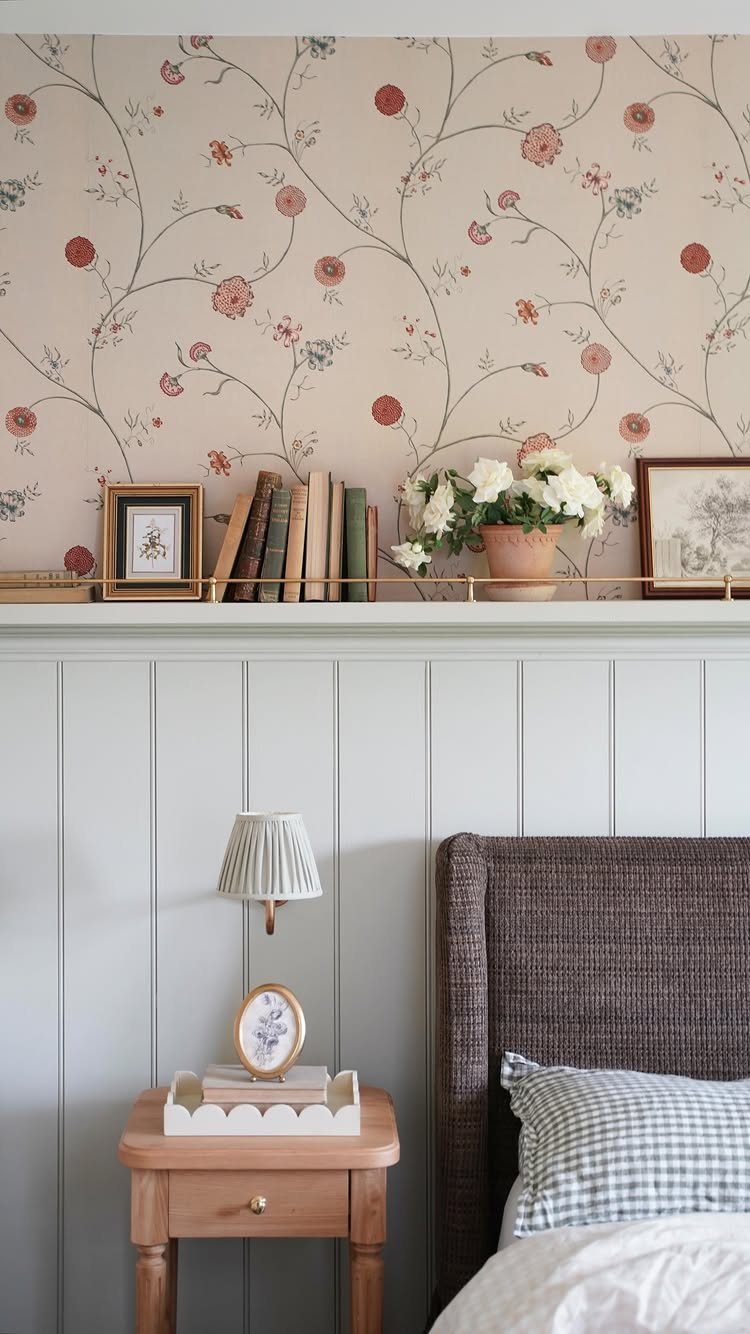 Floral patterned wallpaper above light blue wood paneling with a gold shelf holding decor.