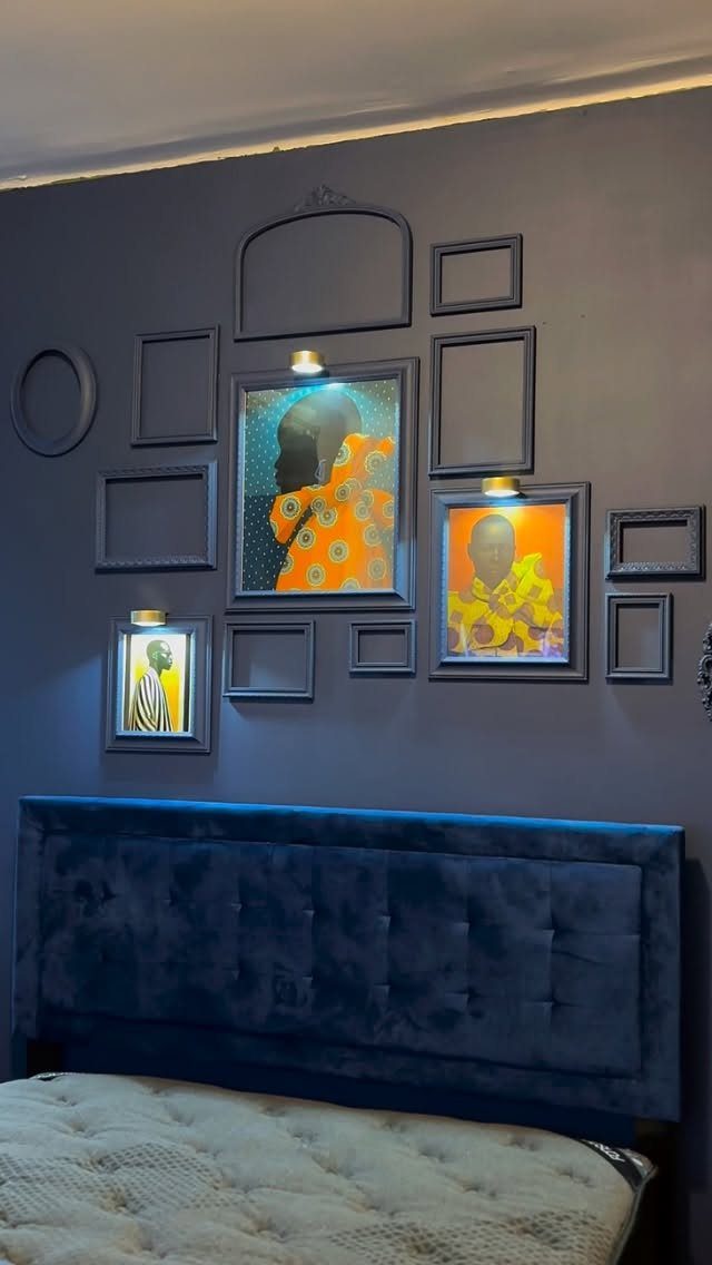 Gallery wall with various black frames and colorful portraits on a dark blue bedroom wall.