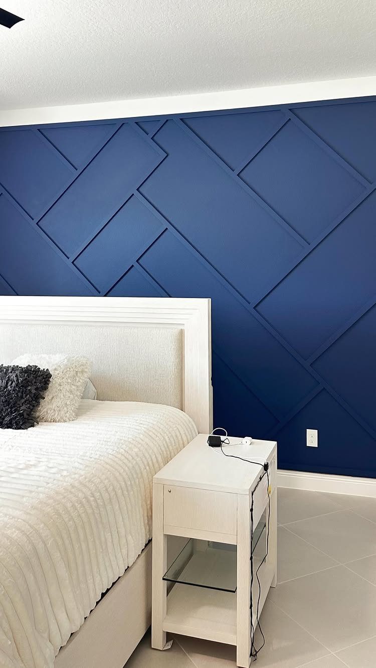 Navy blue bedroom accent wall with a raised geometric rectangular pattern behind a white bed.