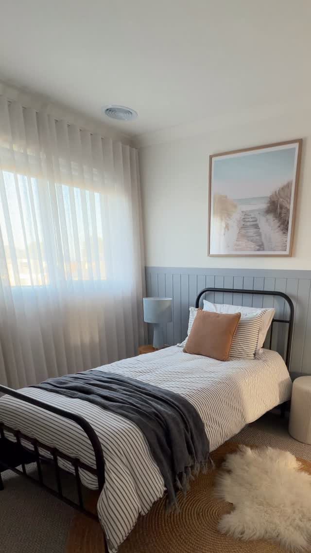 A single bed with striped linens sits against a wall with grey wainscoting.