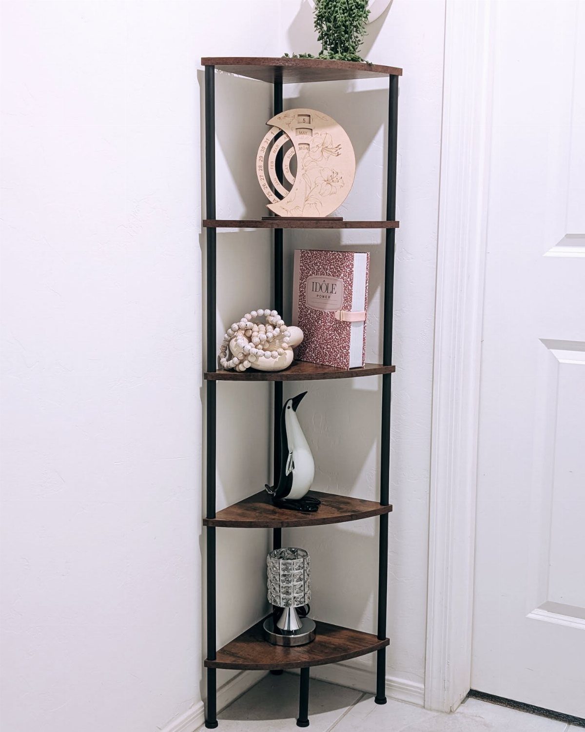 Black iron ladder-style corner shelf with wooden tiers holding various decorative objects in a room corner.