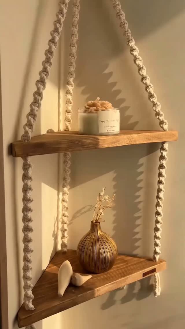 Macrame hanging corner shelves with wooden planks holding a candle and a small vase.