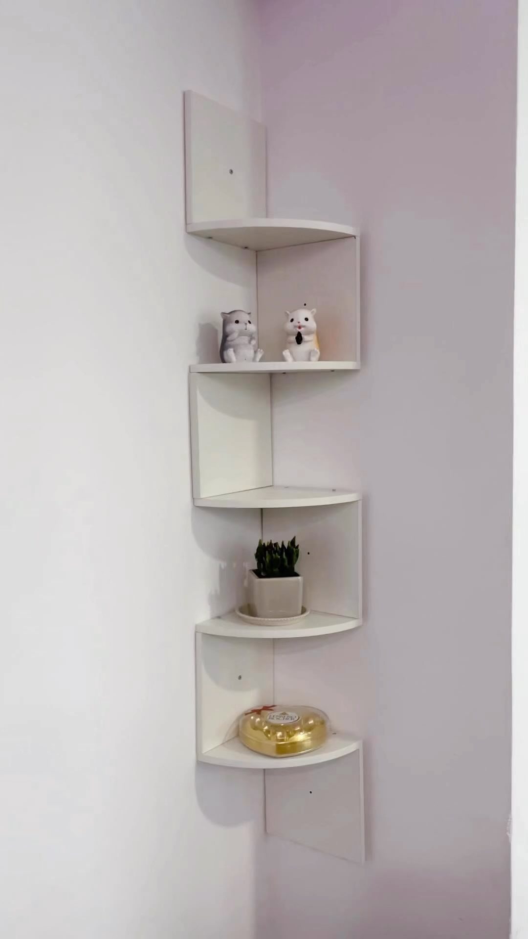 White zig-zag corner shelves holding small figurines, a plant, and a gold container on a wall.