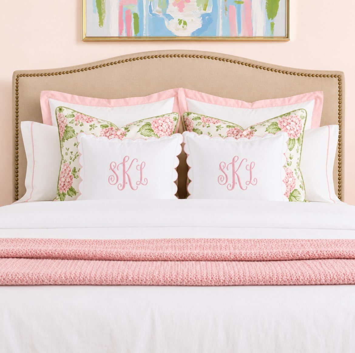 White monogrammed pillows with pink initials rest on a bed with floral accents and pink bedding.