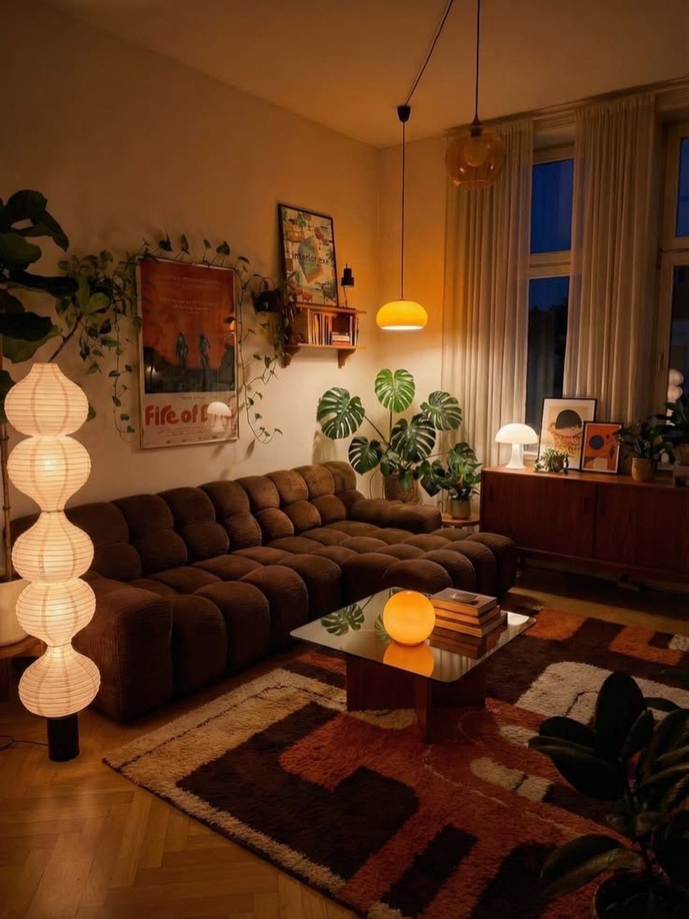 A cozy living room with warm dimmed lighting, a brown sofa, and indoor plants.