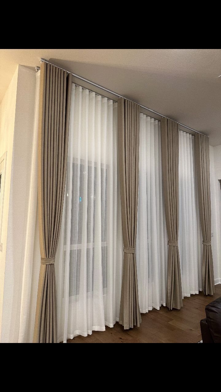 Layered taupe and sheer white curtains hanging from a silver rod over a window.