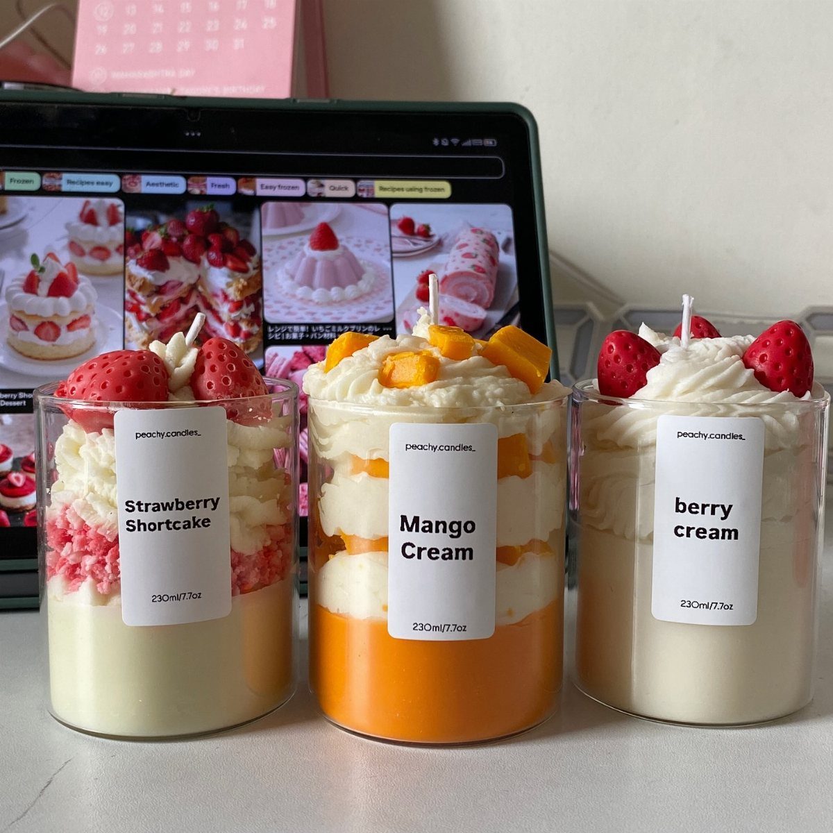 Three dessert-style scented candles in glass jars with fruit-themed toppings and labels.