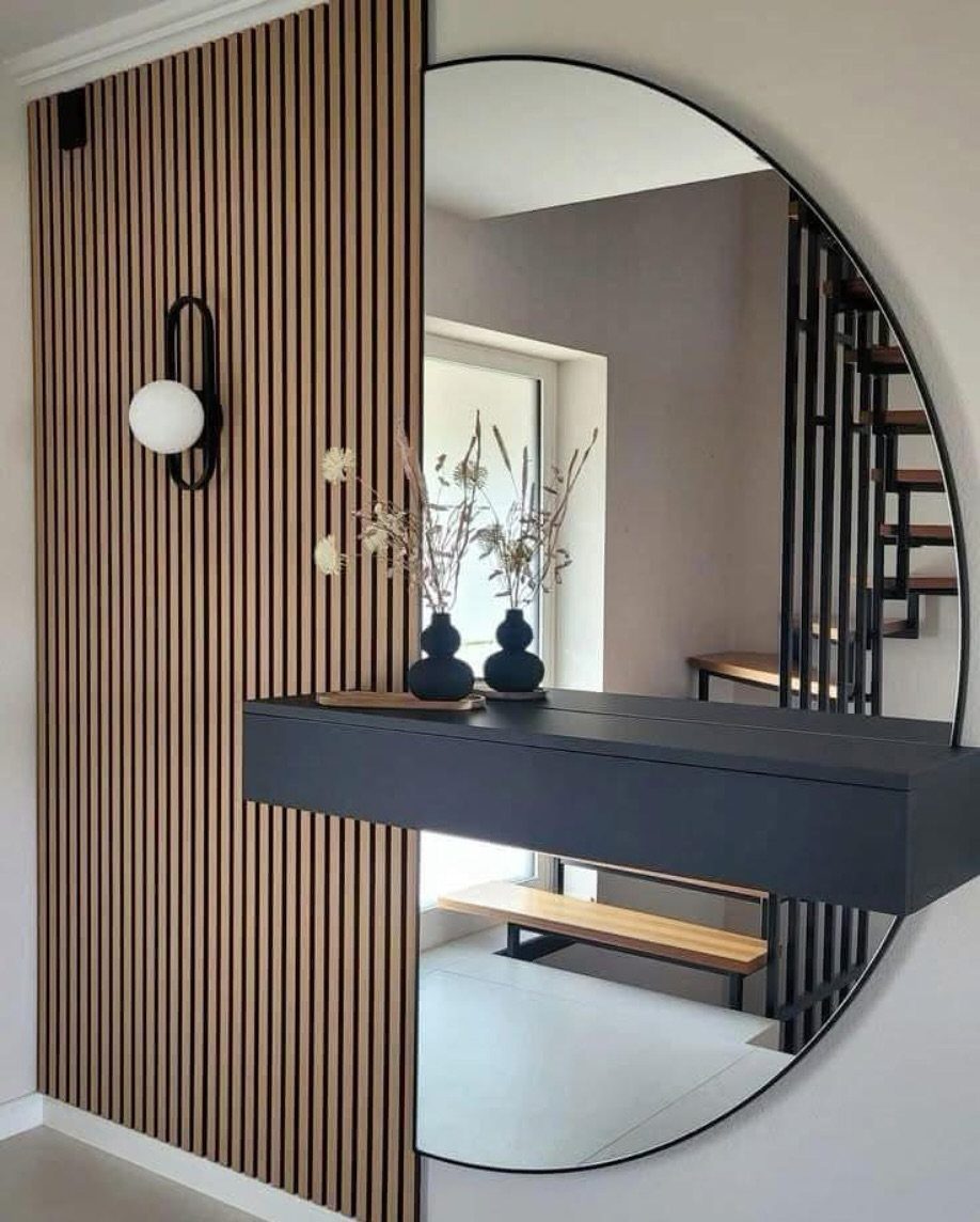 Large round mirror reflecting a modern interior with a black console and wooden accents.
