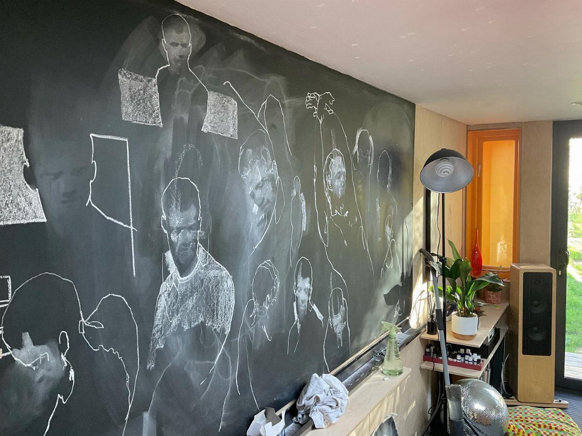 Chalk drawings of human portraits on a large black chalkboard wall in a room.