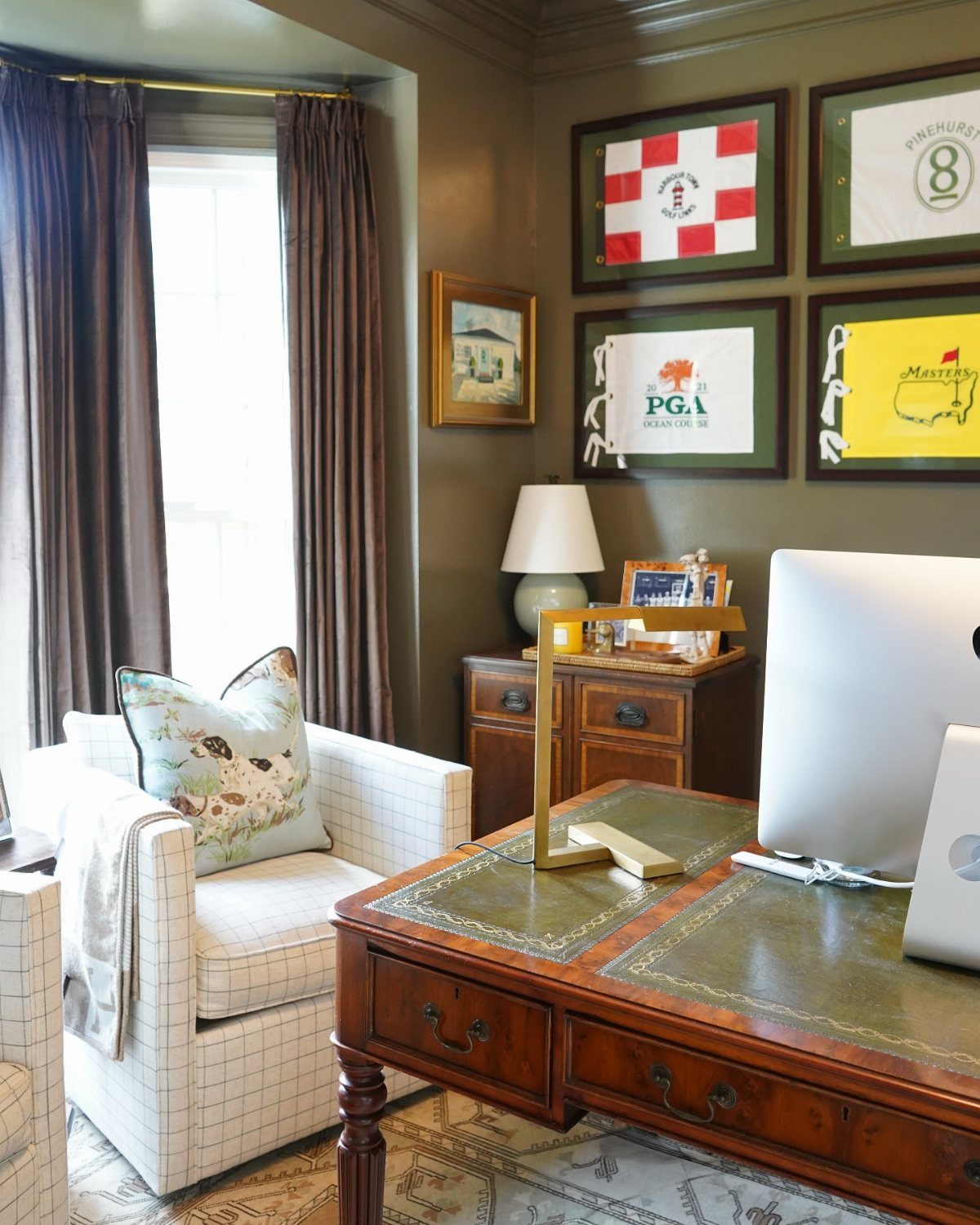 Four framed sports flags hanging on an olive green wall above a wooden desk.