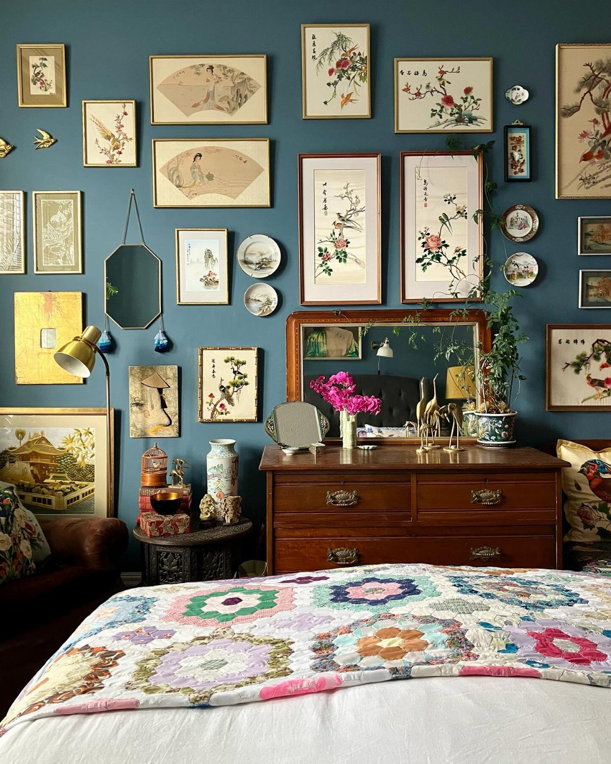 Various framed botanical artworks and decorative plates arranged on a teal bedroom wall.