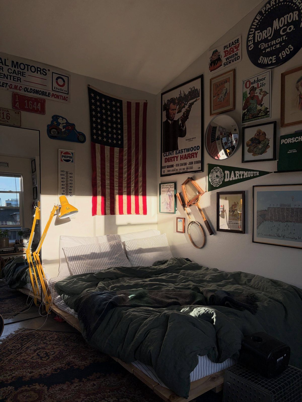 Bedroom wall decorated with an American flag, framed art, and vintage signs above a bed.