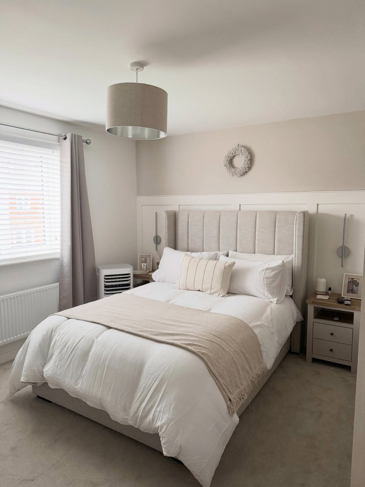 A cozy bedroom with cream bedding, a beige headboard, and soft grey walls.