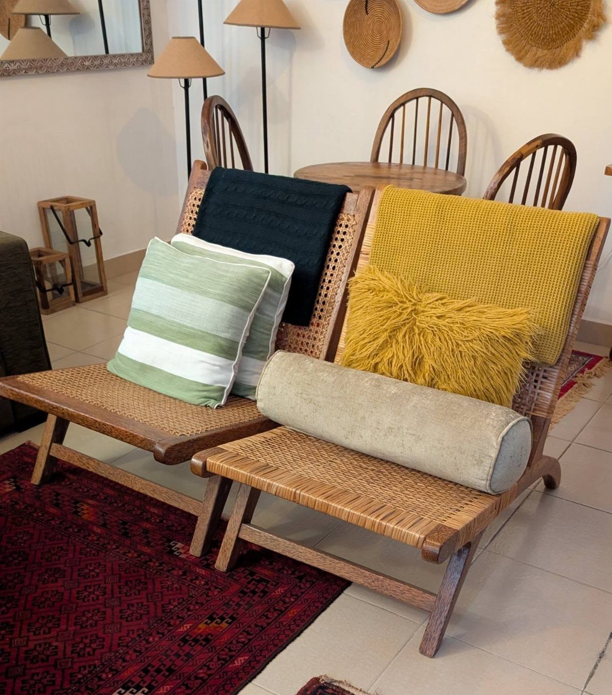 Two woven cane accent chairs with colorful decorative pillows on a red patterned rug.