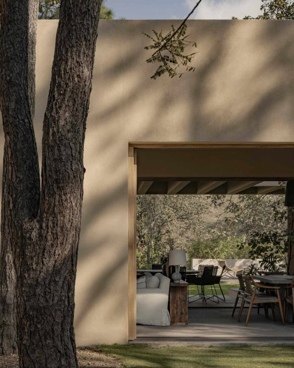 Beige building exterior with an open doorway revealing a patio with wooden furniture and a white sofa.