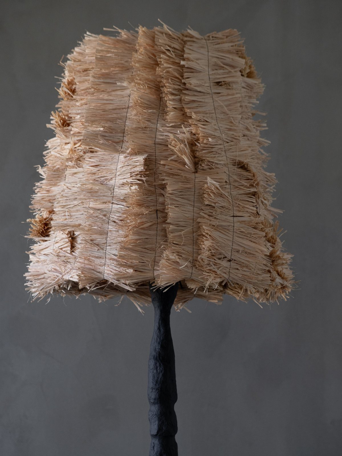A beige textured straw lampshade on a dark sculptural floor lamp stand.