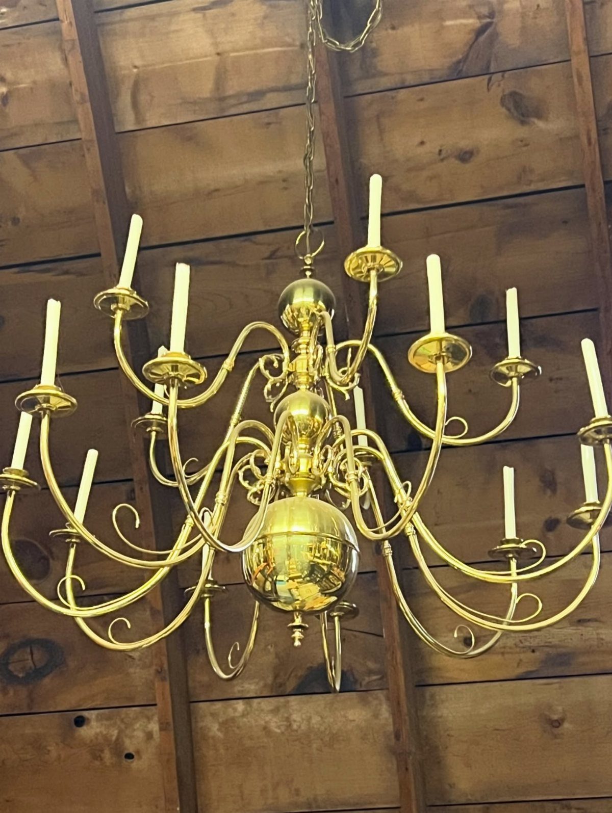Ornate brass chandelier with candle bulbs hanging from a rustic wooden ceiling.